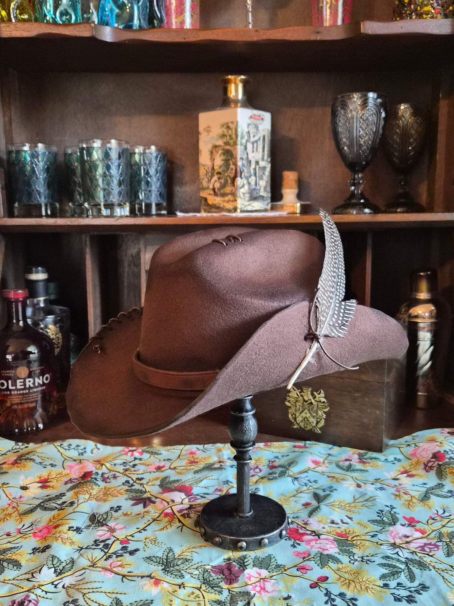 Distressed brown wool fedora with one side of brim tacked up with leather cord and speckled feather accent