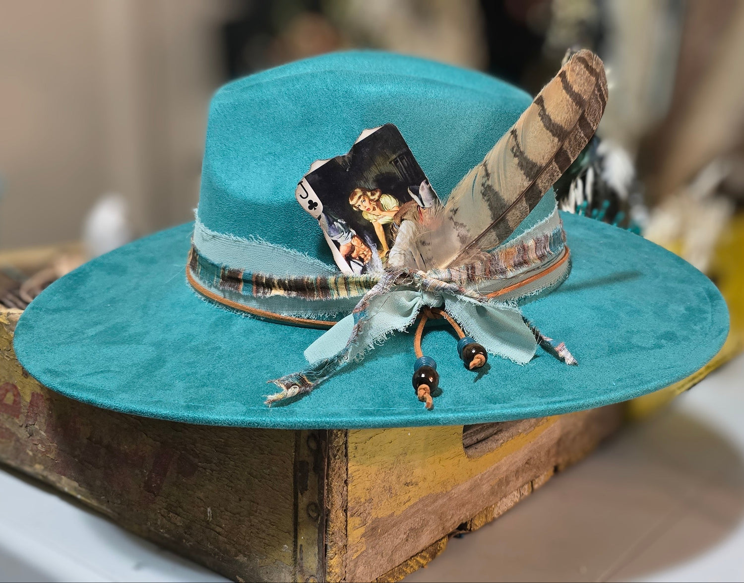 Teal hat with decorative feather and ribbon on a wooden surface for Hat Bar in Memphis, TN